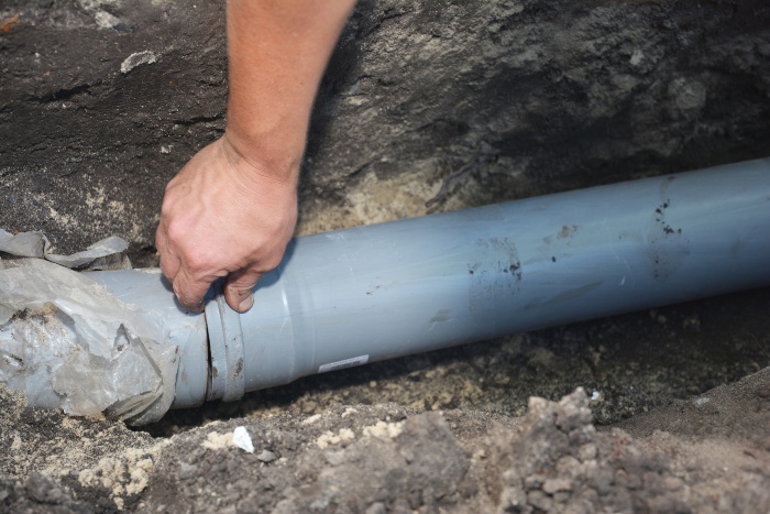 A technician is inspecting a damaged sewer pipe in soil, a common issue in Naperville, IL